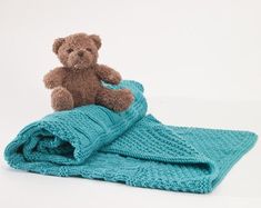 a brown teddy bear sitting on top of a blue knitted blanket with the end rolled up