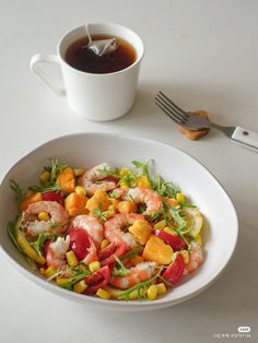 a white bowl filled with shrimp and veggies next to a cup of tea