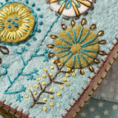 a close up of a cell phone case made out of felt and fabric with embroidered designs