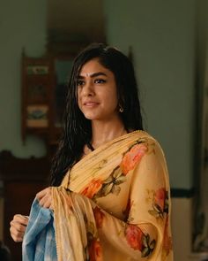 a woman in a yellow sari is holding a blue jacket and looking off to the side