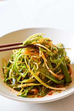 a white bowl filled with green vegetables and chopsticks