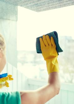 a woman in green shirt and yellow gloves cleaning window sill with microfibrel