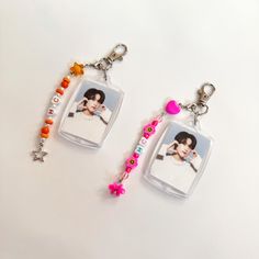 two key chains with pictures and beads hanging from them on a white surface, one is holding a camera