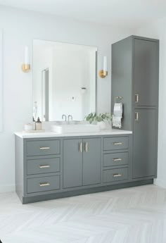 a large bathroom with two sinks and gray cabinetry on the wall, along with gold handles