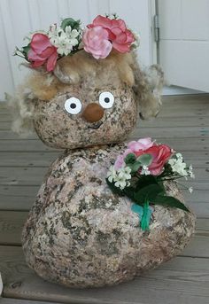 a stuffed animal with flowers on it's head sitting on top of a rock