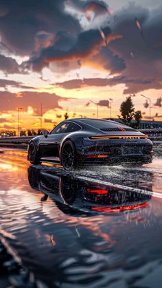 a black sports car is driving on the wet road at sunset with clouds in the background