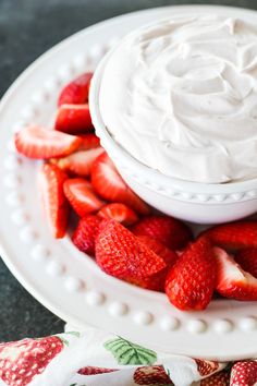 a plate with strawberries and whipped cream on it, next to a small white bowl