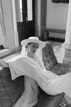 a woman sitting on top of a couch wearing a white hat and long dress,