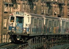 a train is traveling down the tracks in front of some tall buildings and graffiti on the windows