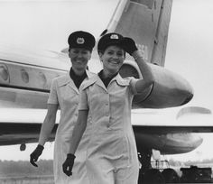 two women in flight uniforms standing next to an airplane with the pilot's cap on