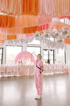 a woman in pink jumpsuits standing under some hanging lights and decorations at a party