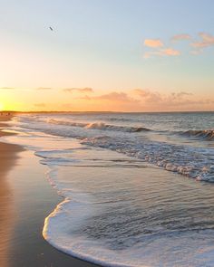 the sun is setting at the beach with waves coming in