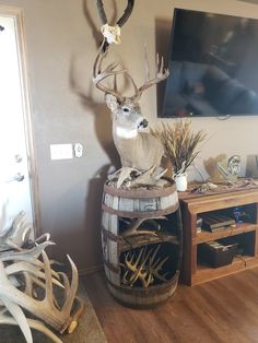 a deer statue sitting on top of a wooden barrel next to a wall mounted tv