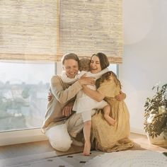 a man and woman hugging each other in front of a window with bamboo shades on the windowsill