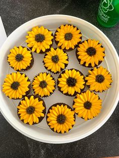 cupcakes decorated with yellow sunflowers in a white bowl next to a green bottle