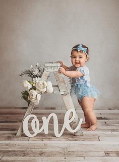 a baby girl standing in front of a wooden sign with the word one on it