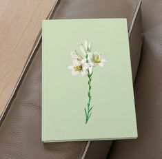 a book with a flower painted on it sitting on a leather couch next to a pillow