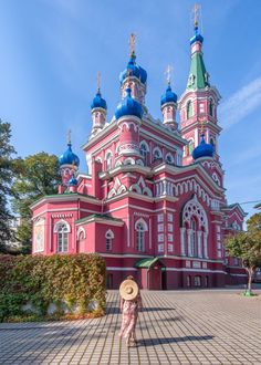 a woman wearing a hat standing in front of a pink building with blue domes on it