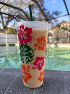 a starbucks drink sitting on top of a table next to a swimming pool with flowers painted on it