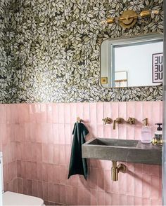 a bathroom with pink and green wallpaper, gold faucet, sink and mirror