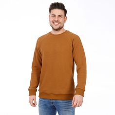 a man standing in front of a white background wearing a brown sweater and blue jeans