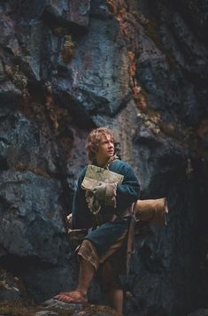 a young boy dressed in medieval clothing sitting on a rock