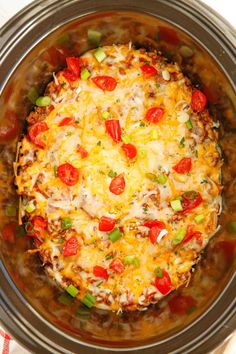 a crock pot filled with cheese, tomatoes and other toppings on top of a table