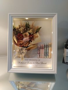 a bouquet of flowers is framed in a white frame on a table next to some books