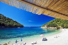 a beach with umbrellas and chairs on it next to the ocean in front of a thatched roof