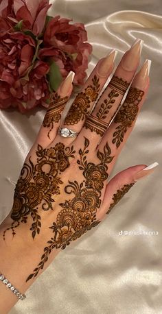 a woman's hand with henna tattoos on it and flowers in the background