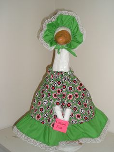 a doll is wearing a green dress and white bonnet with flowers on it, sitting on a shelf