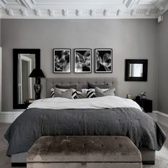 a bedroom with gray walls and pictures on the wall above the bed, along with a bench