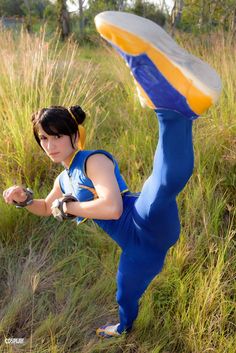 a woman in blue jumpsuit holding a frisbee while standing on one leg