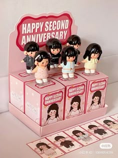 some little figurines are sitting on top of a pink box that says happy second anniversary