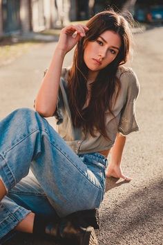 a young woman sitting on the ground with her hand in her hair and looking at the camera