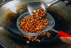 a person scooping peanuts into a frying pan