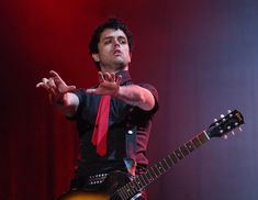 a man in black shirt and red tie playing an electric guitar with his hands out