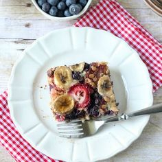 a white plate topped with a piece of fruit cake next to a bowl of blueberries