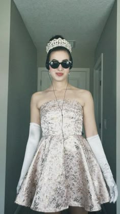 a woman wearing sunglasses and a tiara is standing in a hallway with her hands on her hips