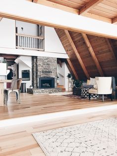 an open living room and dining area with wood floors, exposed beams and stone fireplace