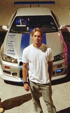 two men standing next to each other in front of a white car with blue stripes