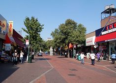 people are walking down the street in front of shops and businesses on a sunny day