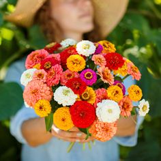 a woman holding a bouquet of flowers in front of her face and wearing a hat