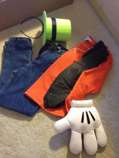 an assortment of clothing sitting on the floor next to a green cup and two white gloves