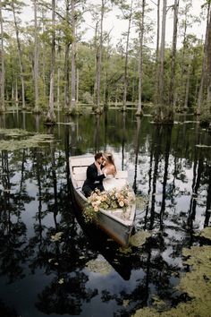 a bride and groom kissing in a rowboat on the water surrounded by tall trees