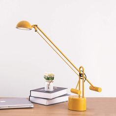 a yellow lamp sitting on top of a wooden desk next to a laptop and flower pot