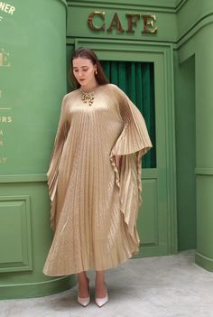 a woman standing in front of a green wall wearing a gold dress with pleated sleeves