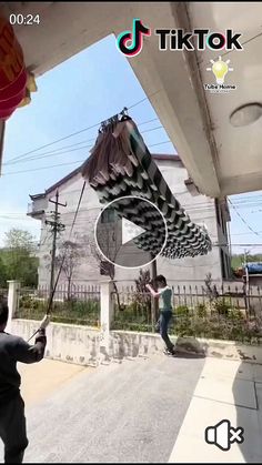 the man is practicing tricks on his skateboard in front of an old building with a giant kite hanging from it's roof