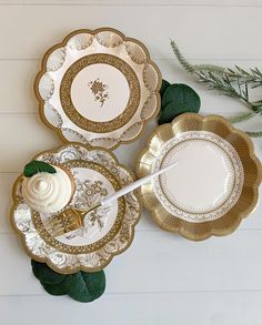 three plates with gold trim and white frosting on them, sitting next to green leaves