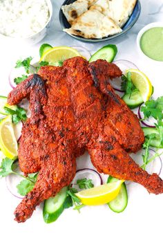 whole roasted tandoori chicken on a plate with cucumbers and lemon wedges